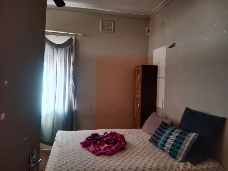 A bedroom featuring a ceiling vent and window with curtain rod, currently showing significant wear to wall finishes and paintwork.
