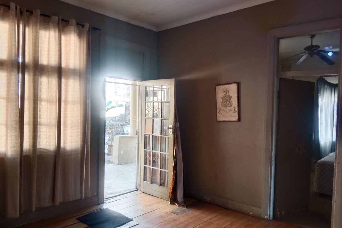 An empty living room featuring original timber flooring, a ceiling fan, and a glass-paneled door providing direct access to an outdoor patio area.