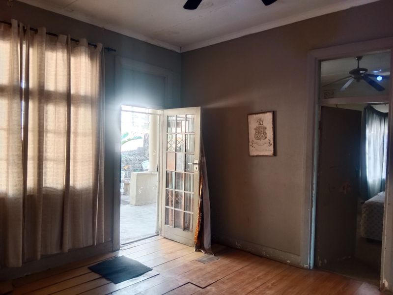 An empty living room featuring original timber flooring, a ceiling fan, and a glass-paneled door providing direct access to an outdoor patio area.