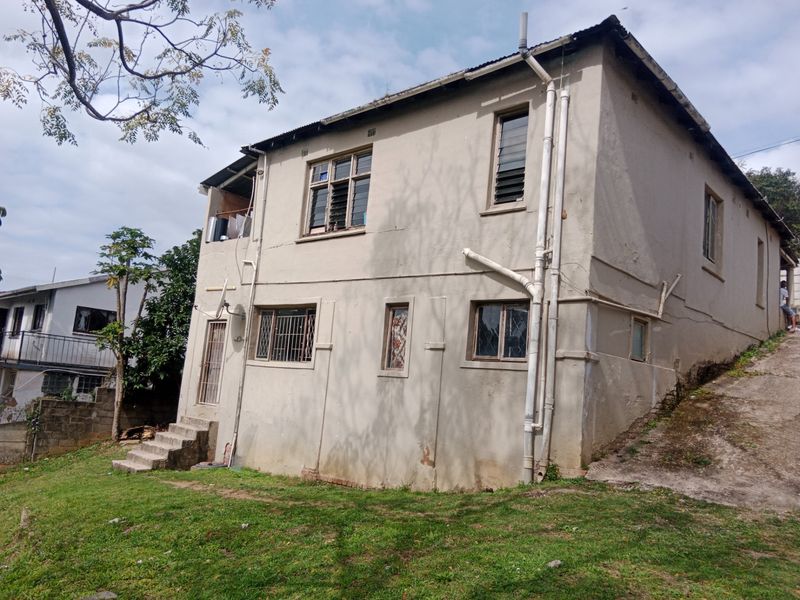 Rear view of a two-story residential property featuring plastered masonry walls, external plumbing, and concrete stairs leading to the garden area.
