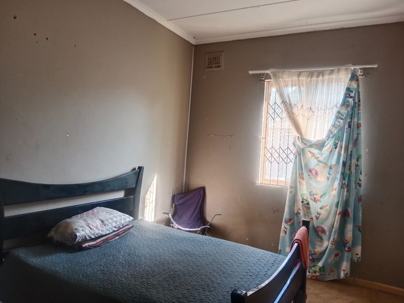 A bedroom featuring a window with a security gate and ventilation brick, requiring cosmetic updates to the wall finishes.