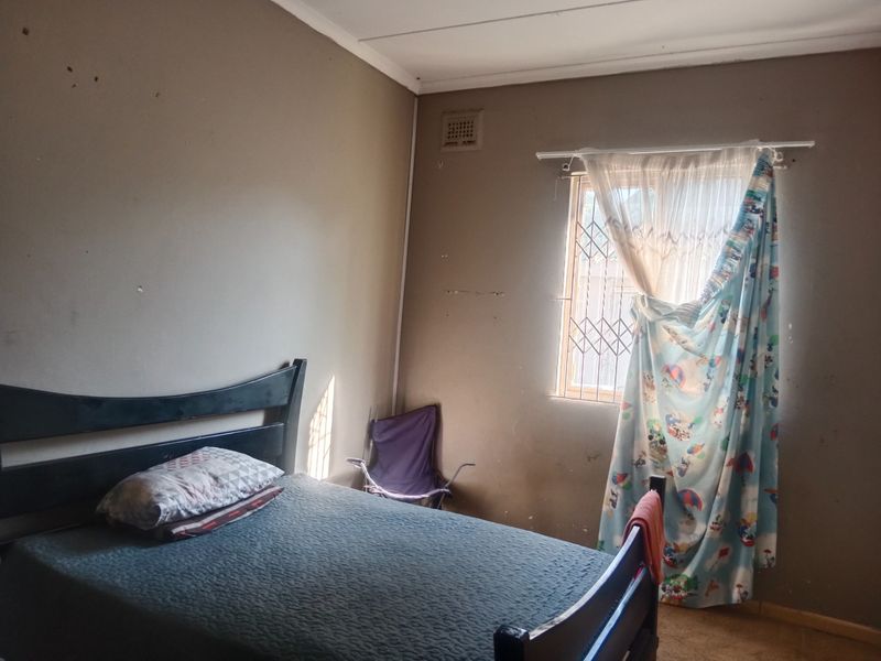 A bedroom featuring a window with a security gate and wall-mounted air vent, requiring cosmetic updates to the wall finishes.