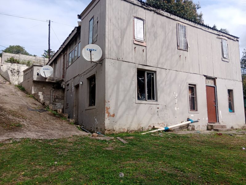 Rear view of a two-story residential building featuring corrugated iron cladding, showing significant signs of exterior wear and maintenance requirements.