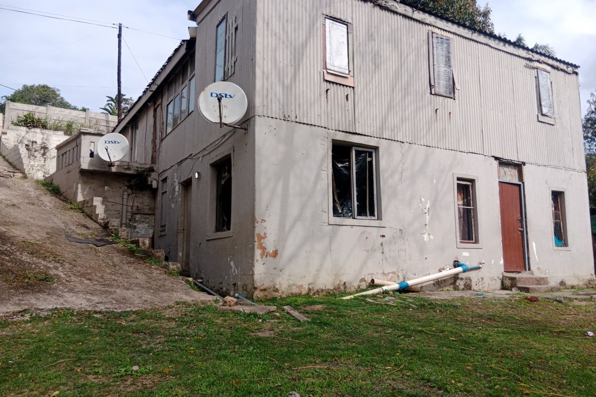 Rear view of a two-story residential building featuring corrugated iron cladding, showing significant signs of exterior wear and maintenance requirements.