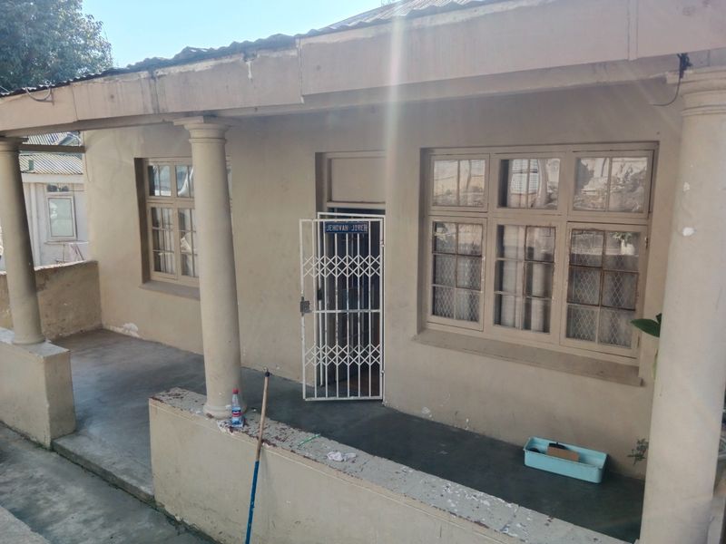 A covered front patio area featuring concrete columns, a security gate, and multi-pane windows, showing signs of wear on the exterior finishes.