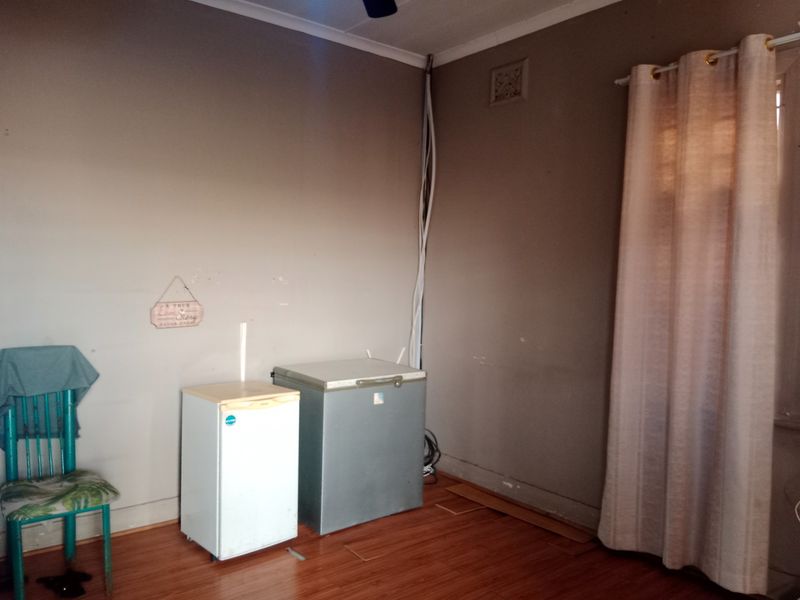 A bedroom featuring laminate flooring and a ceiling fan, currently requiring cosmetic updates and repair to exposed wiring and wall finishes.