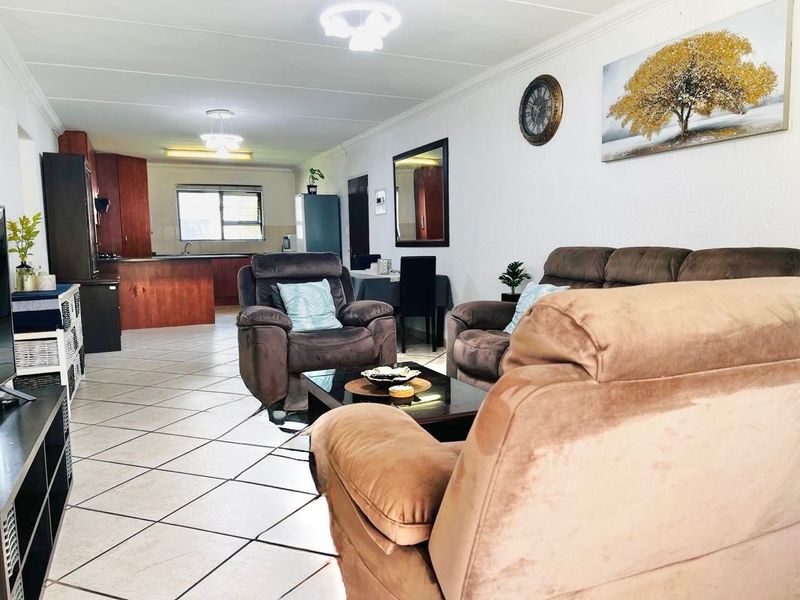 Open-plan living and kitchen area featuring tiled flooring, neutral walls, and functional kitchen cabinetry with a breakfast counter.