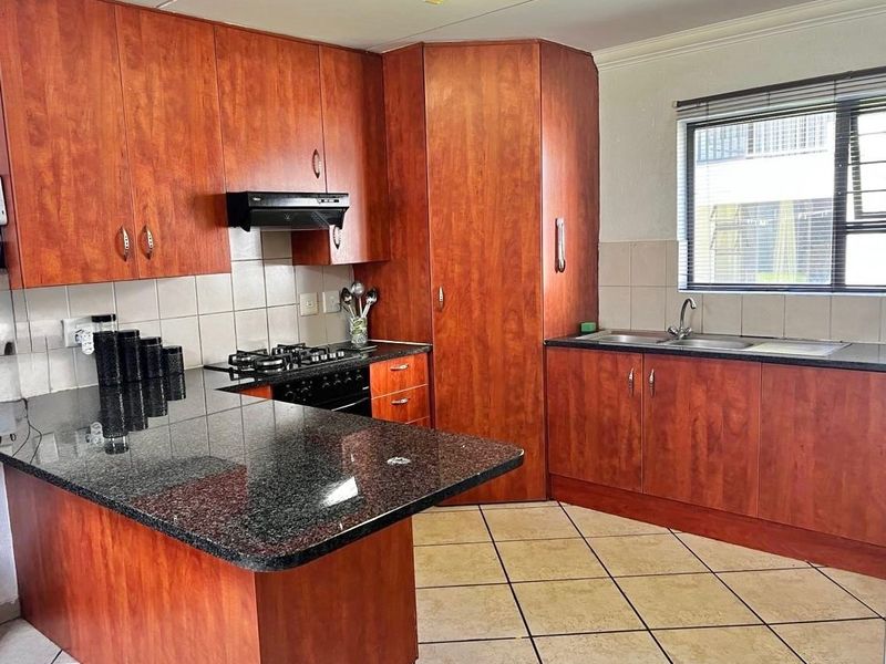 A functional kitchen featuring wood-look laminate cabinetry, granite countertops, a gas hob with extractor, and tiled flooring.