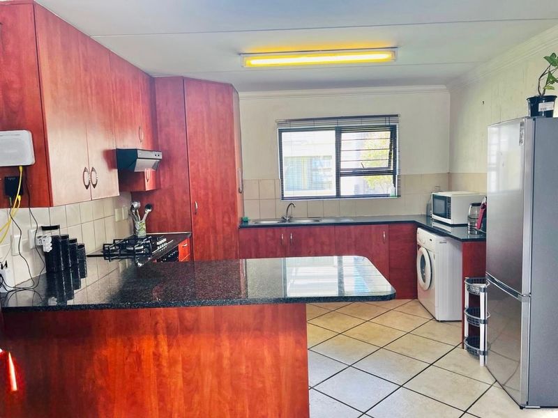 Functional kitchen featuring granite countertops, wood-finish cabinetry, gas hob, extractor fan, and tiled flooring with a window overlooking the exterior.