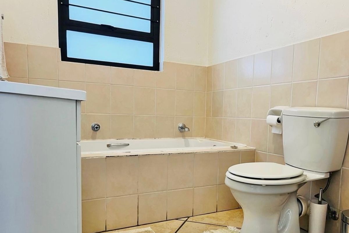 A functional bathroom featuring a built-in bathtub, ceramic tiling, and a standard toilet, offering a blank canvas for potential modernization and renovation.