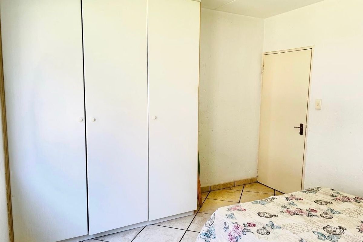 A bedroom featuring built-in cupboards, tiled flooring, and a standard internal door, offering a functional space with potential for cosmetic updates.