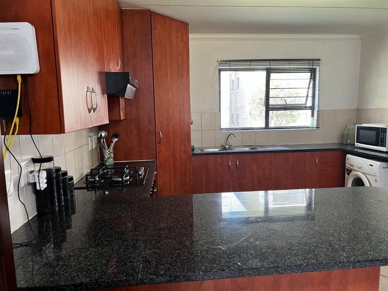 A functional kitchen featuring dark granite countertops, wooden cabinetry, a gas hob, and a tiled backsplash with a window overlooking the exterior.