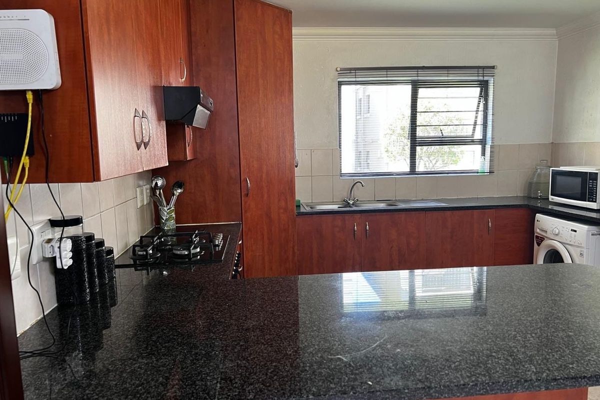 A functional kitchen featuring dark granite countertops, wooden cabinetry, a gas hob, and a tiled backsplash with a window overlooking the exterior.