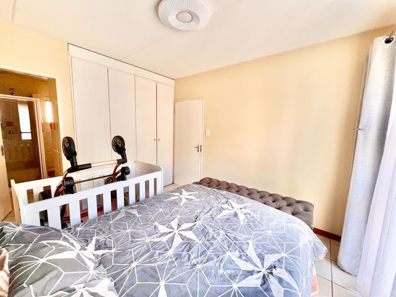 A bedroom featuring built-in cupboards, tiled flooring, and an en-suite bathroom access point, providing a functional and well-lit living space.