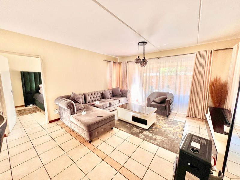 A bright living room featuring tiled flooring, a sliding glass door providing natural light, and modern pendant lighting.