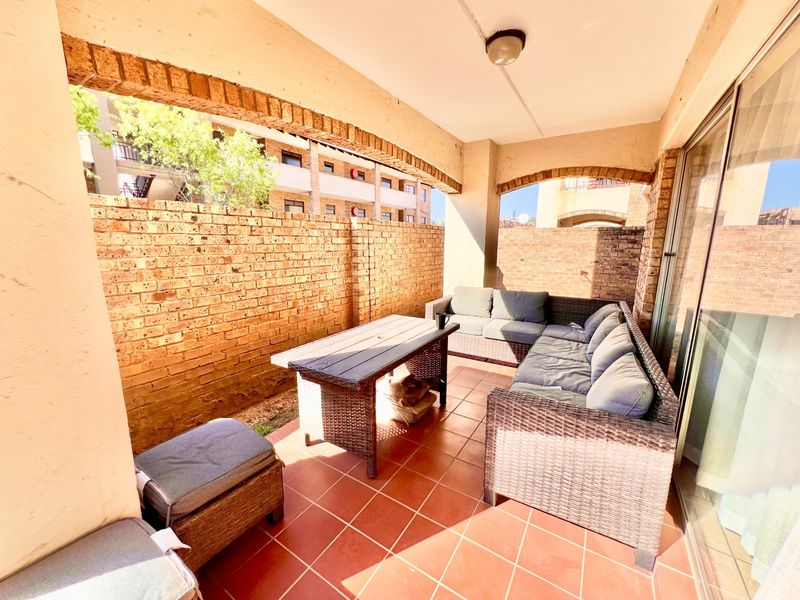 A covered patio area featuring brick wall accents, tiled flooring, and an arched architectural design, providing a functional outdoor living space.