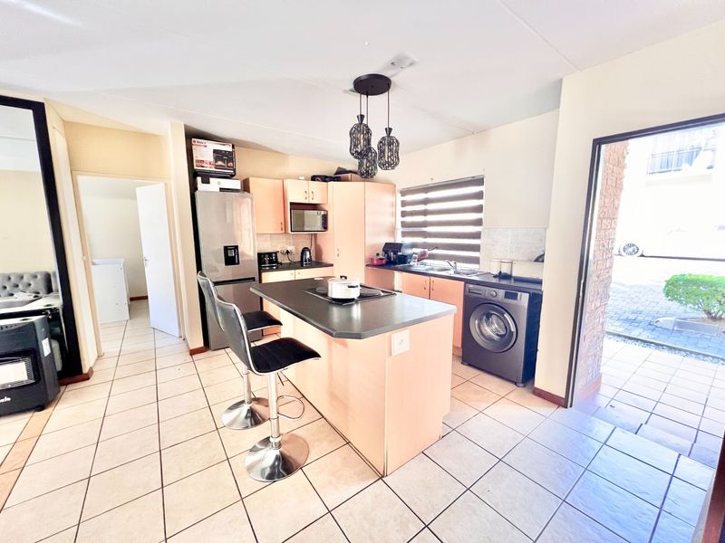 A functional kitchen featuring a central island with a built-in hob, ample cabinetry, tiled flooring, and direct access to the exterior.