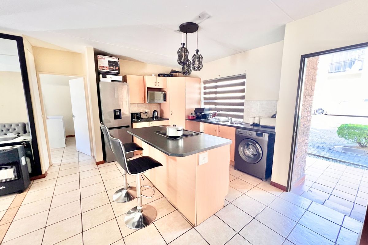 A functional kitchen featuring a central island with a built-in hob, ample cabinetry, tiled flooring, and direct access to the exterior.