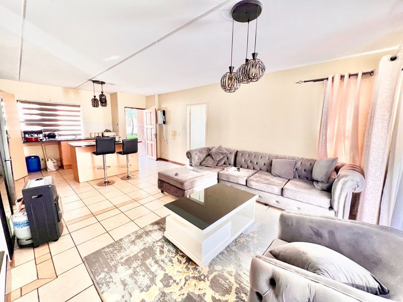 Open-plan living area featuring a kitchen island with breakfast bar seating, ceramic tiled flooring, and modern pendant lighting throughout the combined space.