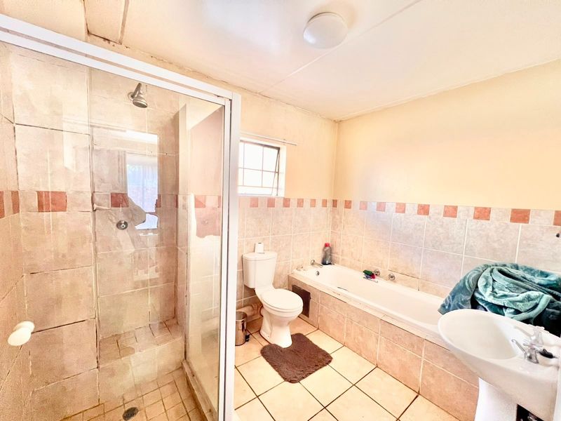 A dated bathroom featuring a shower enclosure, built-in bathtub, pedestal basin, and toilet with neutral wall and floor tiling.