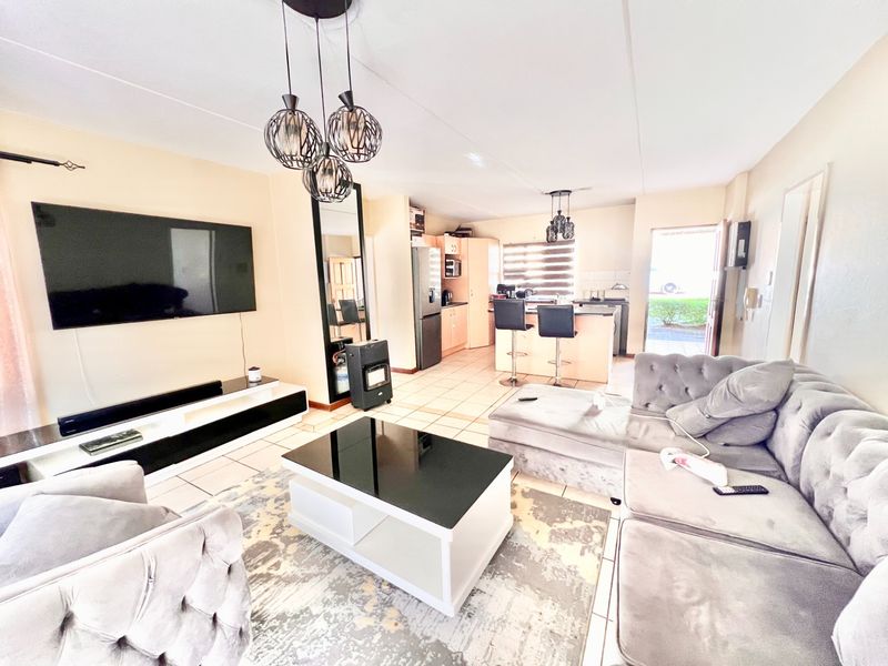 An open-plan living and kitchen area featuring tiled flooring, modern pendant lighting, and a functional kitchen island with built-in cabinetry.