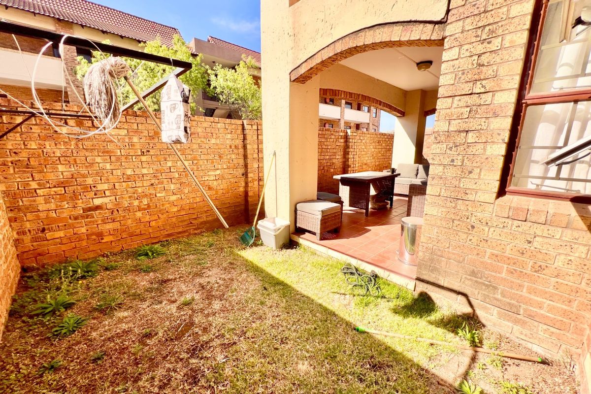 A rear exterior view featuring a small private garden with a brick boundary wall and a covered tiled patio area.