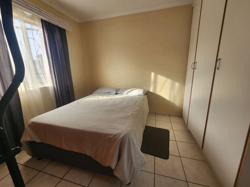 A functional bedroom featuring built-in cupboards, tiled flooring, and natural light through a window with security bars.