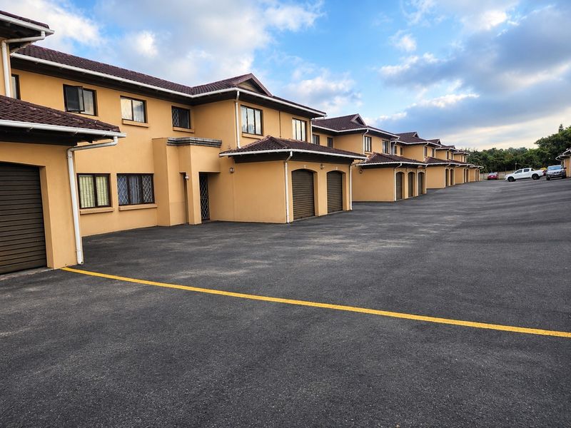A row of residential townhouses featuring tiled roofs, multiple garage doors, and a large paved driveway area.