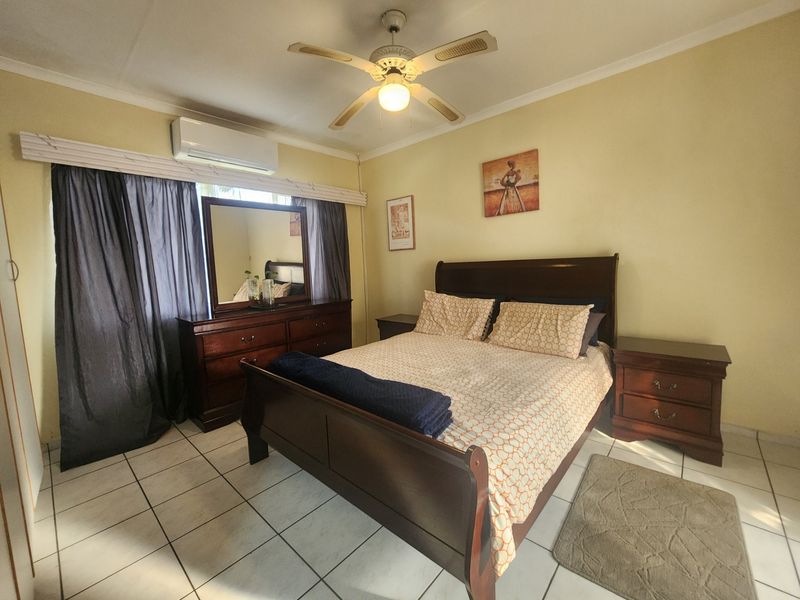 A well-maintained bedroom featuring ceramic floor tiles, a ceiling fan, and a wall-mounted split-system air conditioning unit.
