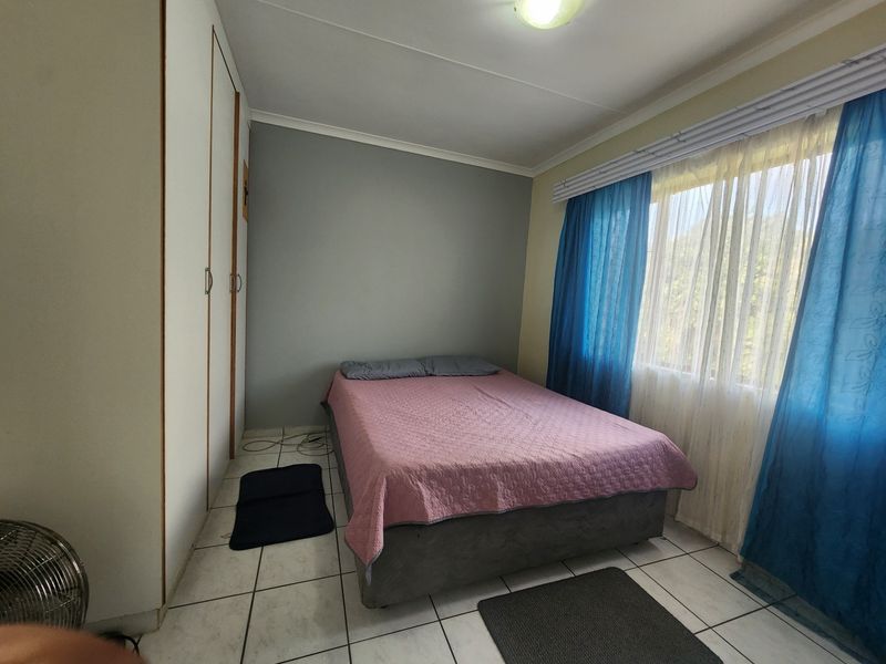 A functional bedroom featuring built-in cupboards, tiled flooring, and a window with natural light.