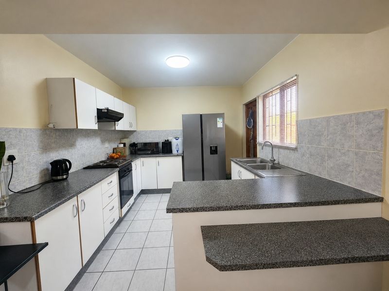 Functional kitchen featuring white cabinetry, dark laminate countertops, tiled backsplash, built-in oven, gas hob, and a double basin sink with a breakfast nook.