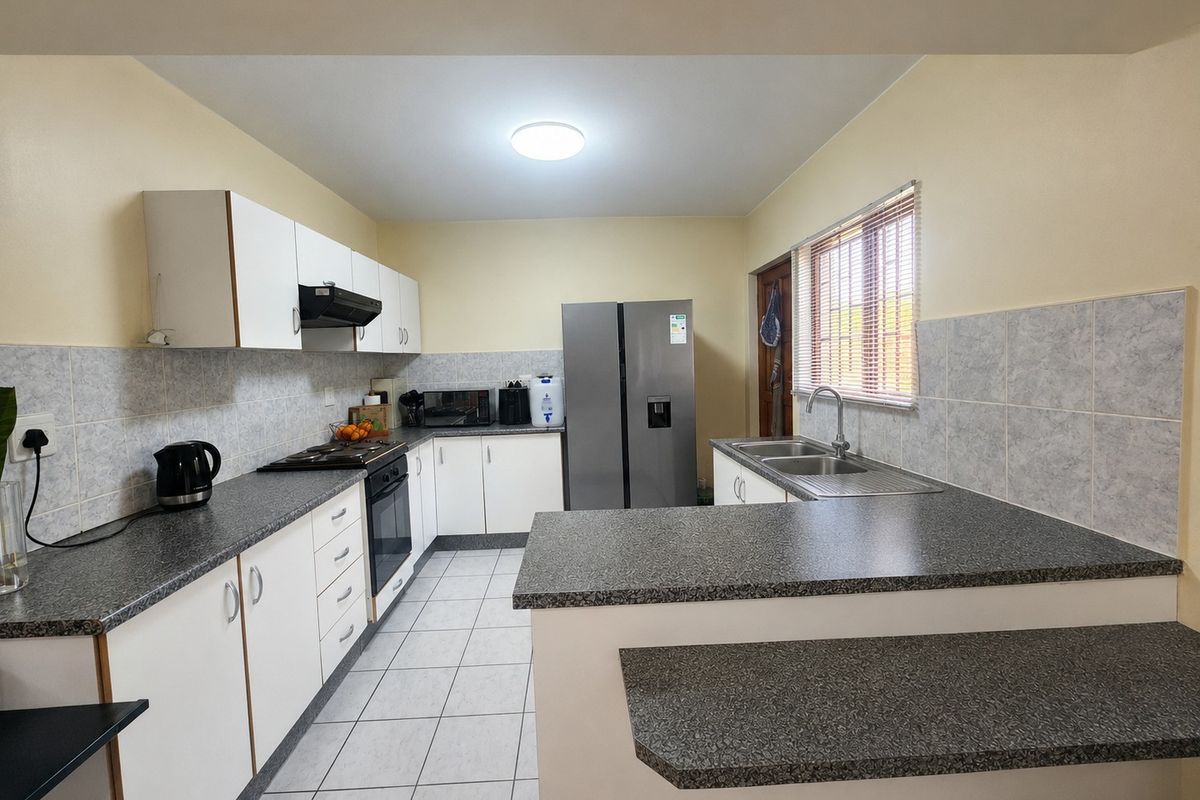 Functional kitchen featuring white cabinetry, dark laminate countertops, tiled backsplash, built-in oven, gas hob, and a double basin sink with a breakfast nook.
