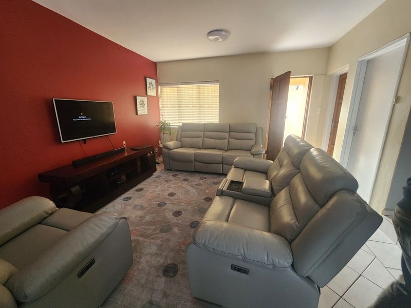 A comfortable living room featuring tiled flooring, a bold red accent wall, and natural light through venetian blinds.