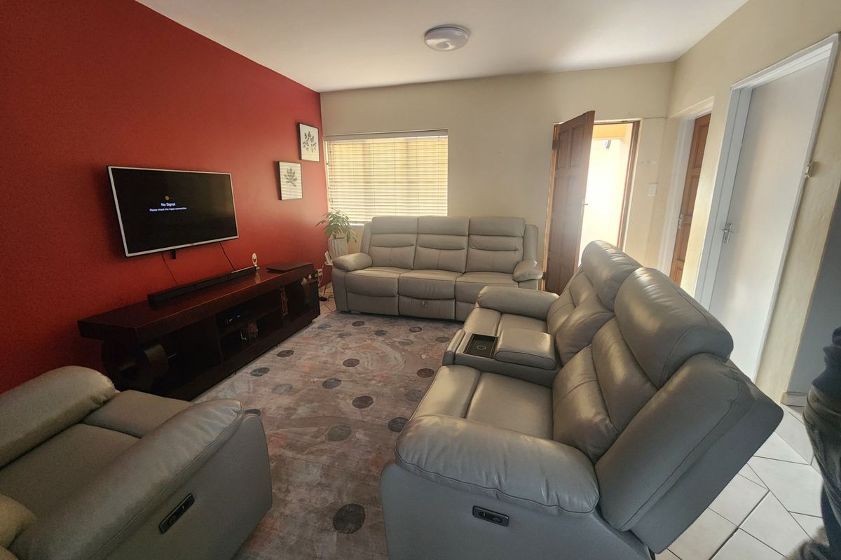 A comfortable living room featuring tiled flooring, a bold red accent wall, and natural light through venetian blinds.