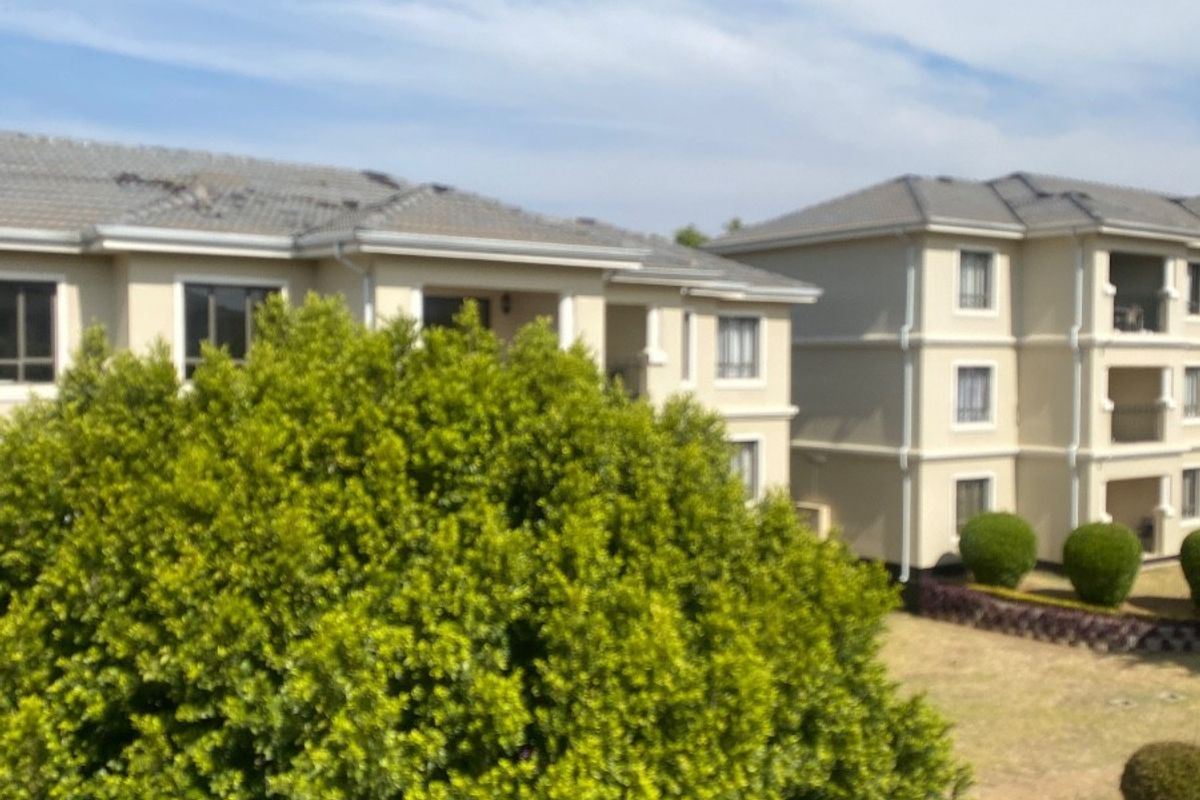 Exterior view of apartment complex buildings featuring tiled roofs, balconies, and surrounding landscaped garden areas.
