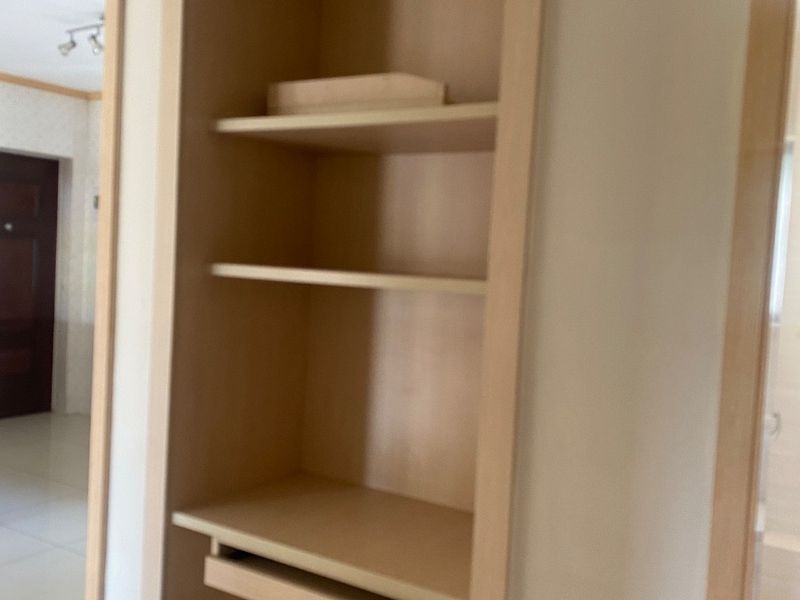 A hallway featuring a built-in wooden shelving unit with integrated electrical outlets and neutral tiled flooring.