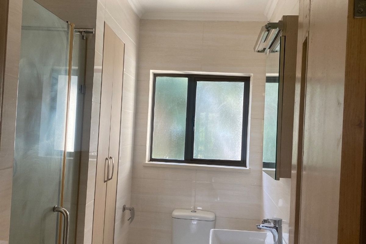 A clean, modern bathroom featuring a glass shower enclosure, a vanity with a ceramic basin, and neutral wall and floor tiling.