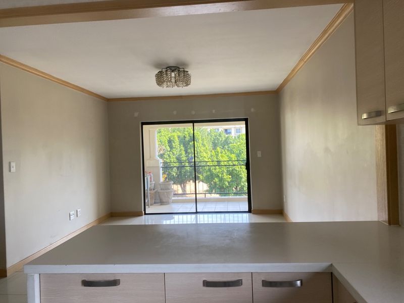 An open-plan living and kitchen area featuring neutral cabinetry, crown molding, and a sliding glass door leading to a balcony.