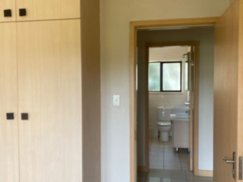 A hallway featuring built-in cupboards with light wood finish, leading into a tiled bathroom area.