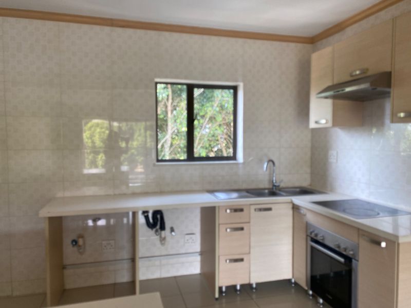 A functional kitchen featuring light wood-finish cabinetry, built-in oven and hob, tiled splashbacks, and a stainless steel sink, currently vacant and ready for updates.