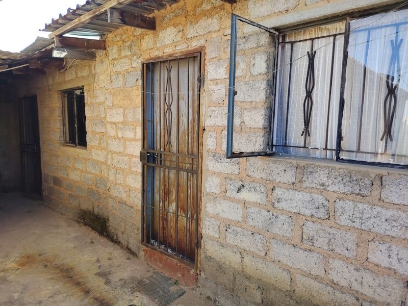Exterior view of a concrete block dwelling featuring metal security gates and window bars with a corrugated metal roof overhang.