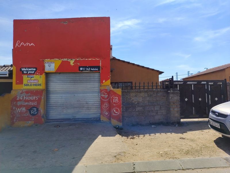 Front elevation of a commercial-style property featuring a metal roller shutter door, perimeter wall with security spikes, and a metal gate.