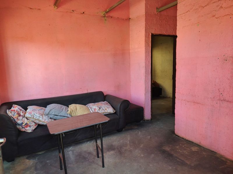 A basic living area featuring unfinished pink walls and exposed ceiling beams, requiring significant renovation to improve the overall condition and aesthetic appeal.
