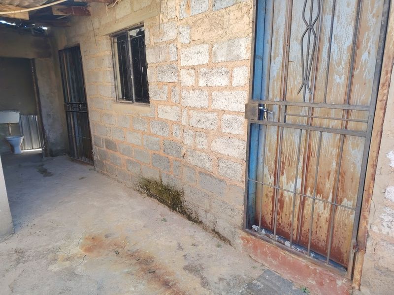 Exterior view of a concrete block structure featuring security gates and windows, showing significant signs of wear and weathering.