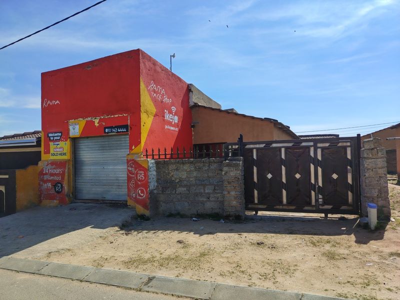 Front elevation of a property featuring a roller shutter door, metal gate, and concrete block boundary wall with visible exterior paint wear.