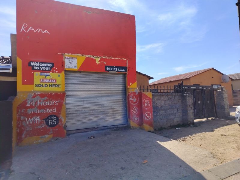Front facade of a commercial or utility structure featuring a metal roller shutter door and a concrete block boundary wall.