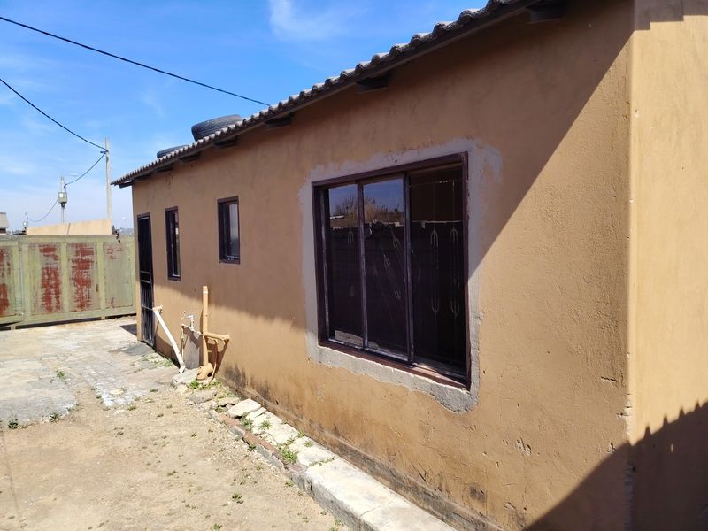 Rear exterior view of the property showing a plastered wall with sliding windows, security bars, and visible exterior plumbing fixtures.