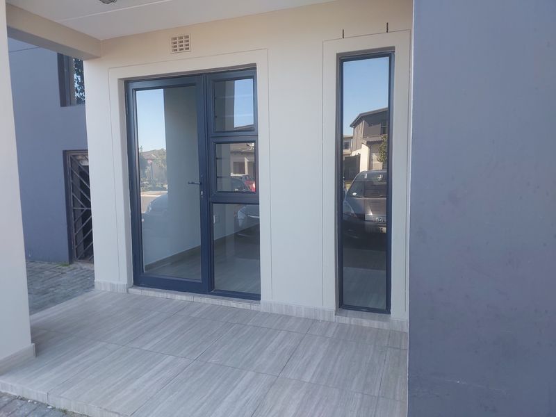 Front entrance area featuring a tiled patio, modern aluminium framed glass door, and a fixed glass sidelight.