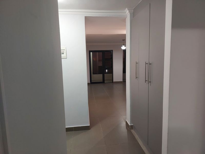 A clean, neutral hallway featuring built-in cupboards, tiled flooring, and a view through to the main living area.