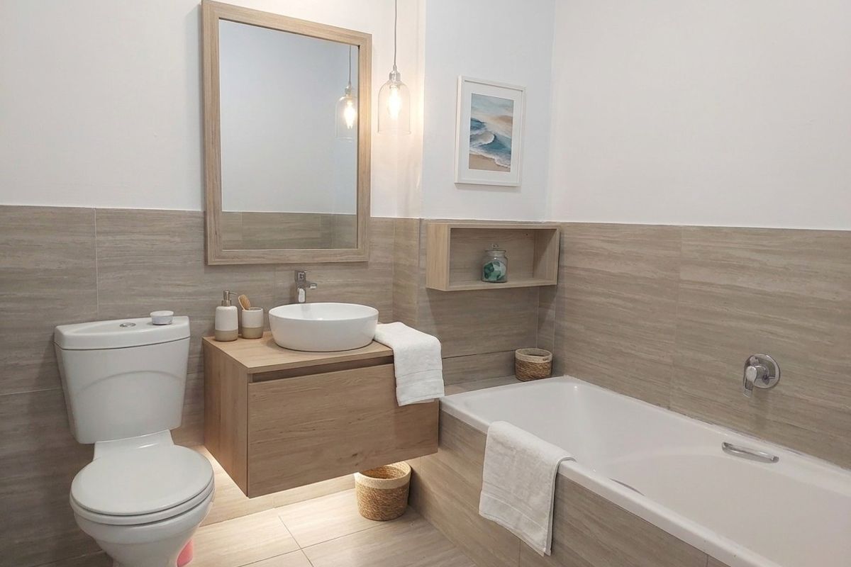 Modern bathroom featuring a wall-mounted vanity with vessel sink, built-in bathtub, and neutral-toned tiled wall finishes.